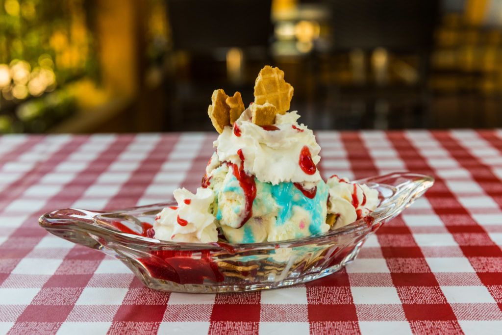 A build-your-own sundae with Scooper's Hero ice cream, strawberry sauce, whipped cream and marshmallows, and crushed waffle cone pieces served in an ice cream boat.
